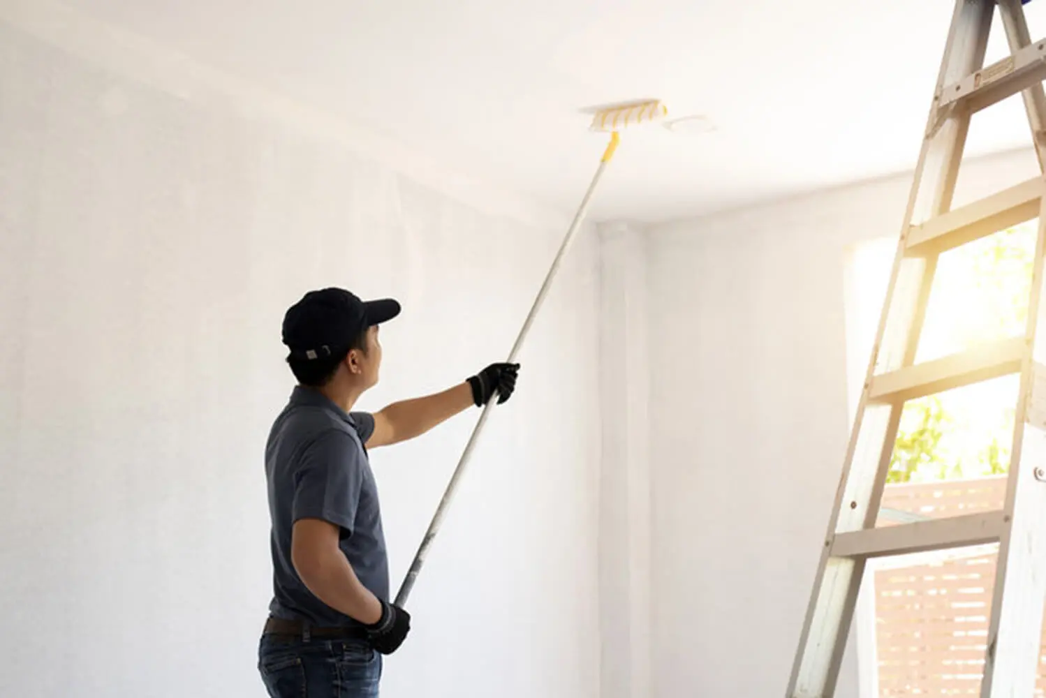 Professional painter using an extension roller to paint an interior ceiling white during a home painting project in Fort Myers.