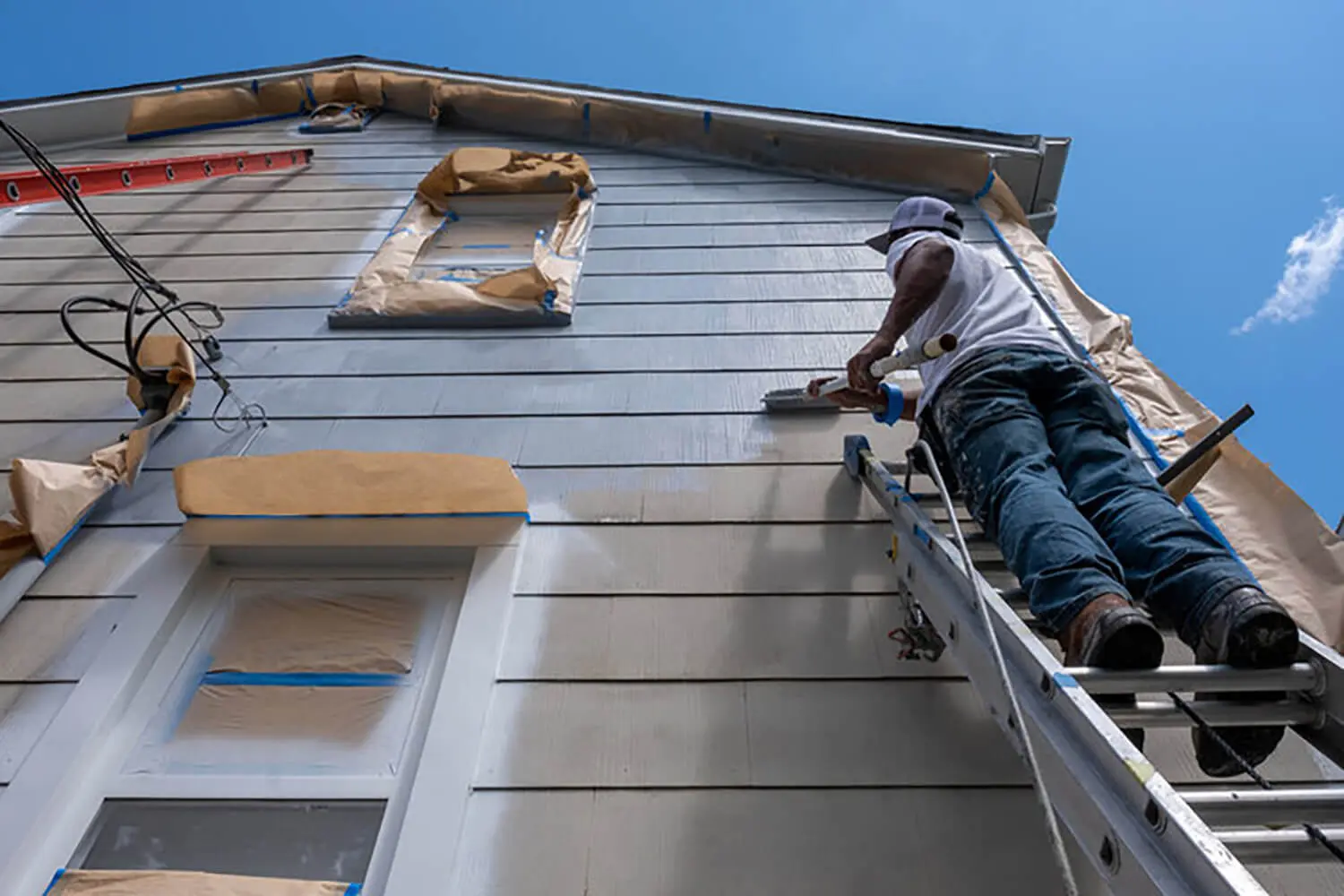 Painter on ladder applying primer to home siding, illustrating what to expect before an exterior painting project starts