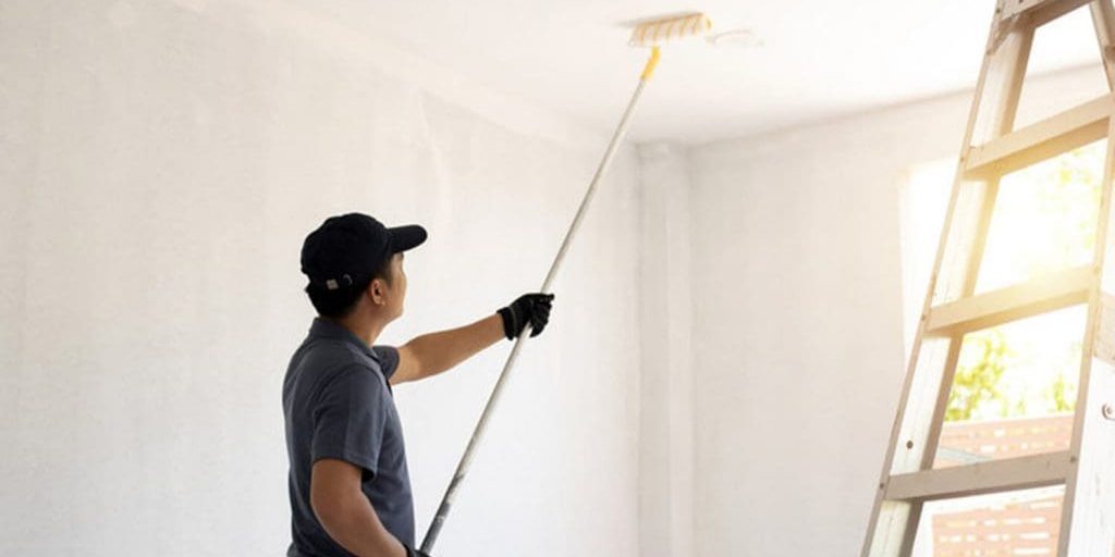 Professional painter using an extension roller to paint an interior ceiling white during a home painting project in Fort Myers.